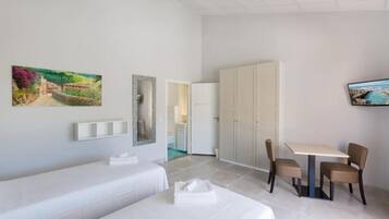 Een hotelkamer met twee eenpersoonsbedden, een eettafel met stoelen, een kledingkast en twee aan de muur hangende schilderijen.