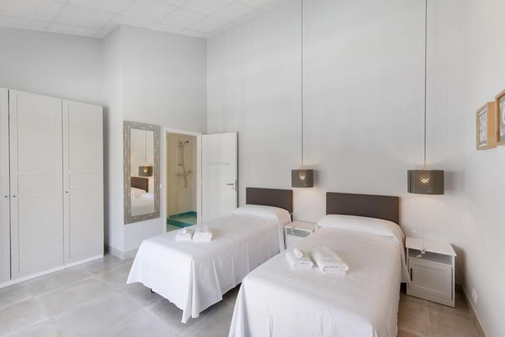 Habitación de hotel con dos camas, un armario, un baño y una mesita de noche con lámpara.
