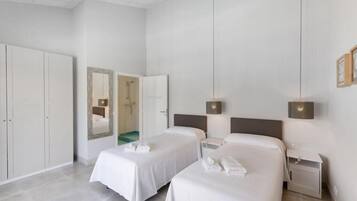 Habitación de hotel con dos camas, un armario, un baño y una mesita de noche con lámpara.