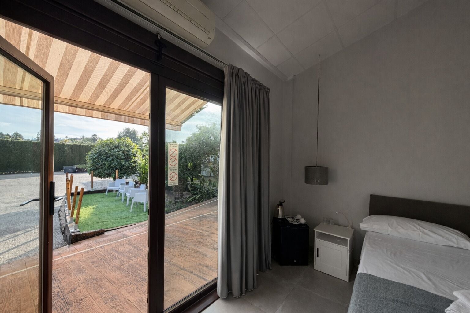 A modern hotel room with a large sliding glass door leading to a patio with outdoor seating and a view of a garden.