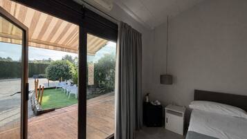 A modern hotel room with a large sliding glass door leading to a patio with outdoor seating and a view of a garden.