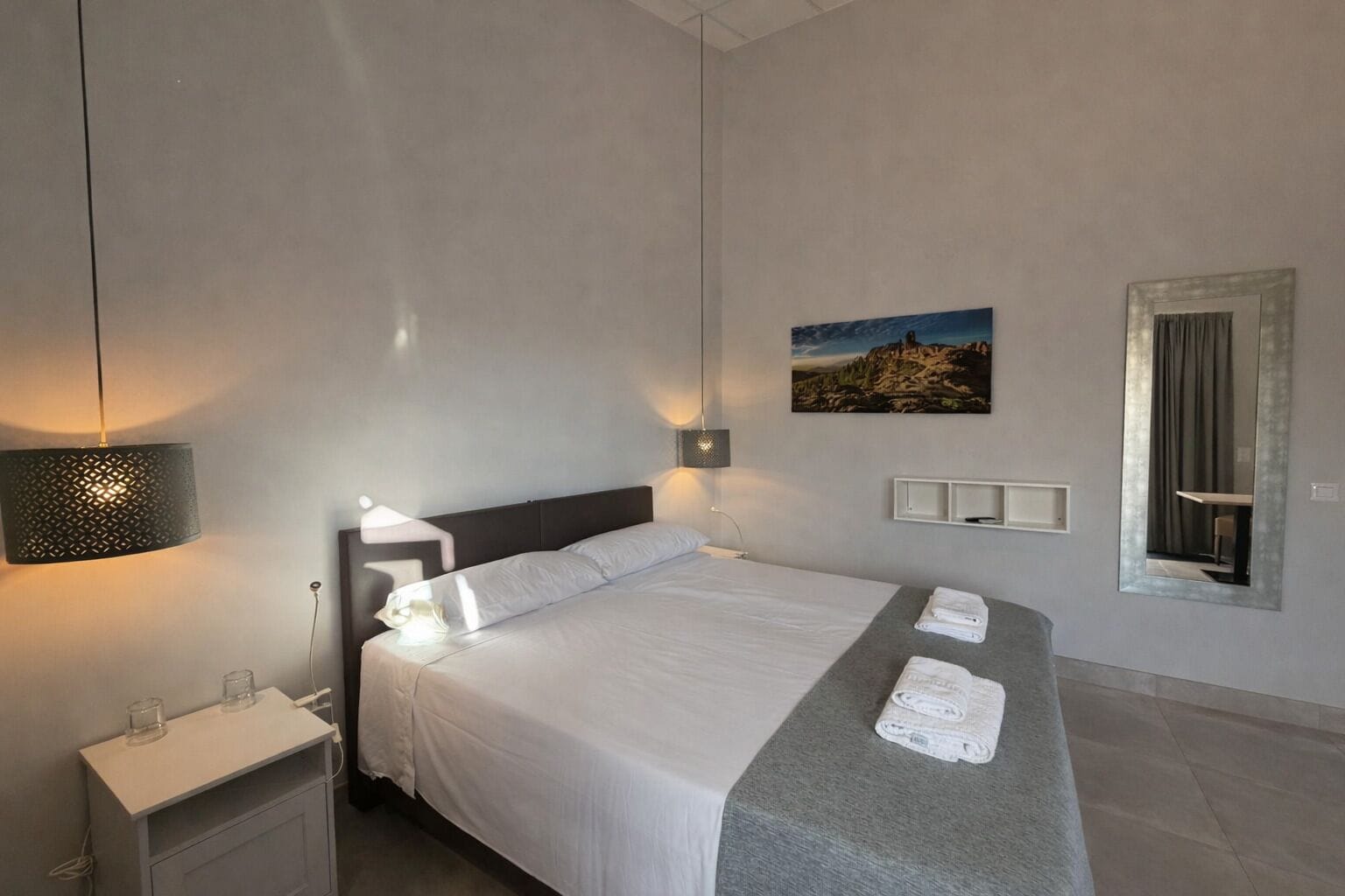 Habitació d'hotel moderna amb un llit gran, làmpades de nit, una petita taula de nit, un mirall i un quadre a la paret.