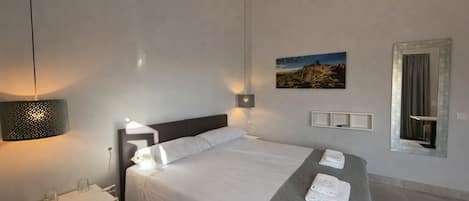 Una habitación de hotel moderna con una cama grande, lámparas de noche, una mesita de noche pequeña, un espejo y un cuadro en la pared.