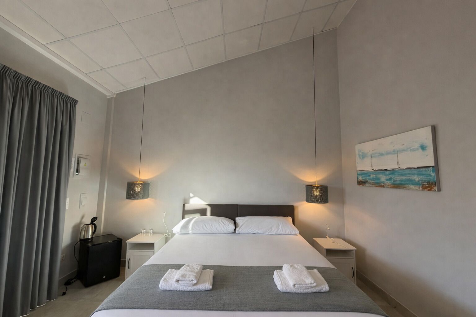 A hotel room with a large bed, two bedside tables, a nightstand, a painting, and a window with curtains.