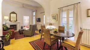 Un coin repas avec une table ronde, des chaises en osier et un tapis rouge à motifs.