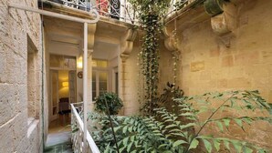 Une cour étroite dotée d’un balcon, de murs en pierre et d’une végétation luxuriante.