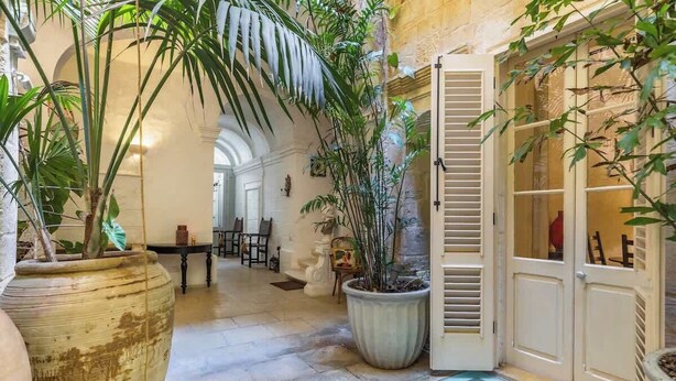 Un vaste atrium doté d’un haut plafond, de grandes plantes en pot et d’une porte en bois de style traditionnel.