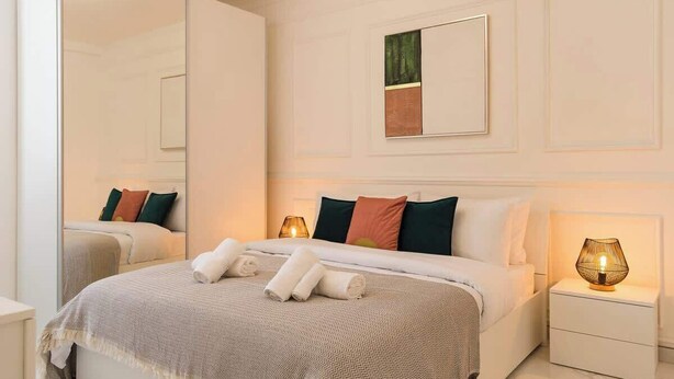 Quarto de hotel moderno com uma cama grande, luminárias de cabeceira e um espelho.