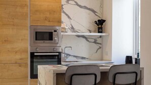 Uma cozinha moderna com micro-ondas embutido, forno e painel de parede em mármore. Há duas cadeiras em uma mesa de jantar pequena.