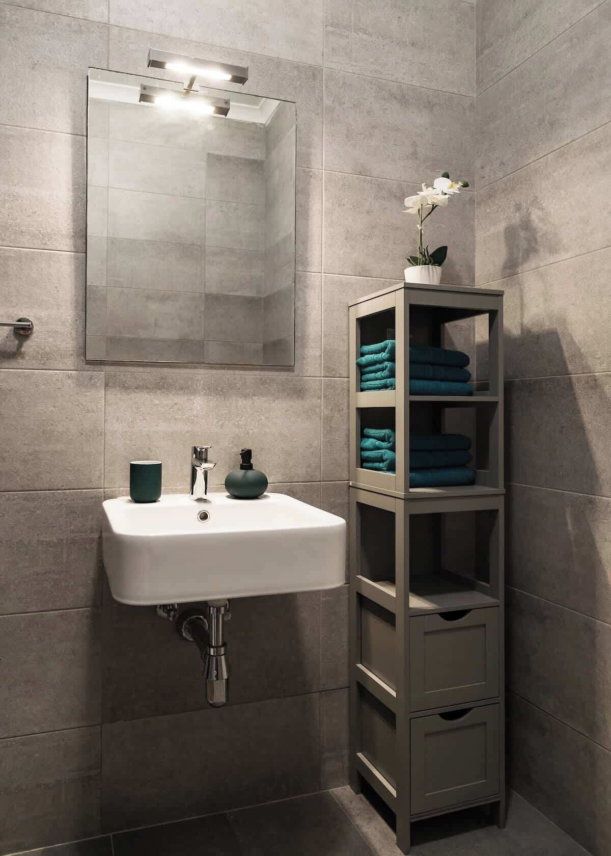 A bathroom with a white sink, a mirror, and a towel rack with folded towels.