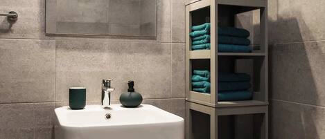 Un baño con lavamanos blanco, un espejo y un perchero con toallas dobladas.