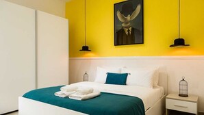 Een moderne hotelkamer met een bed, witte nachtkastjes, een blauwgroene sprei en een gele accentmuur.
