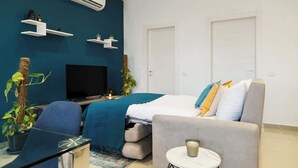 Een moderne hotelkamer met een bed, een televisie, een bureau en een stoel. Er zijn twee witte deuren en een blauwe muur.
