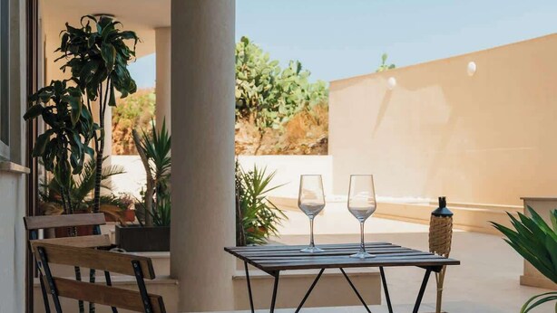 Een terras met een tafel en twee stoelen, een plant in pot en uitzicht over een woestijnlandschap.