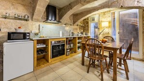 Une cuisine rustique avec des murs en pierre, un four encastré, un four à micro-ondes et des chaises en bois autour d’une table.