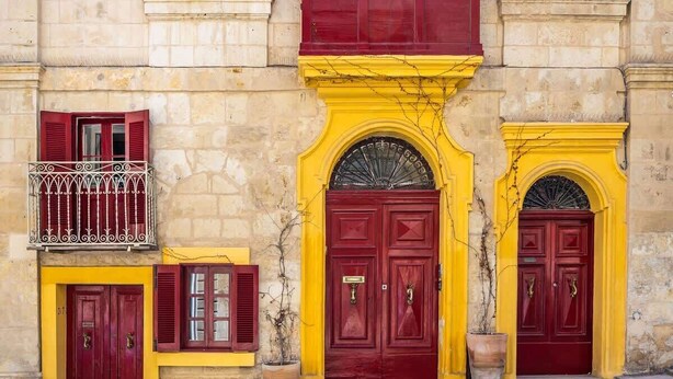 Un immeuble avec trois portes rouges, chacune surmontée d’un petit balcon.