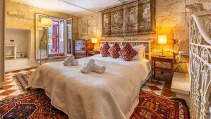 Une chambre d’hôtel avec un grand lit, un mur en pierre, un tableau et une vue sur l’extérieur, visible à travers une porte ouverte.