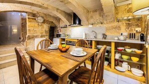 Une cuisine rustique en pierre, avec une table à manger en bois, des chaises et un panier de fruits.
