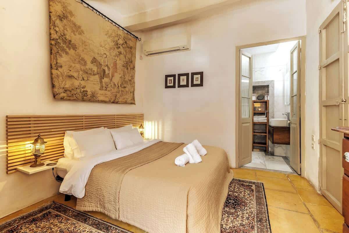 Un dormitorio con cama, lámpara de noche, una obra de arte y vistas al baño.