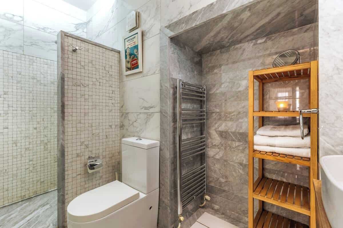 Un baño con ducha, inodoro y un toallero de madera.