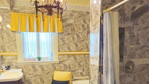 A bathroom with a marble wall, a bathtub, a yellow chair, a chandelier, and a shower curtain. - TTR - Princess Grace (Pembroke)