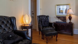 A room with a black leather sofa, a matching armchair, a wooden side table with a lamp, and a framed picture on the wall.