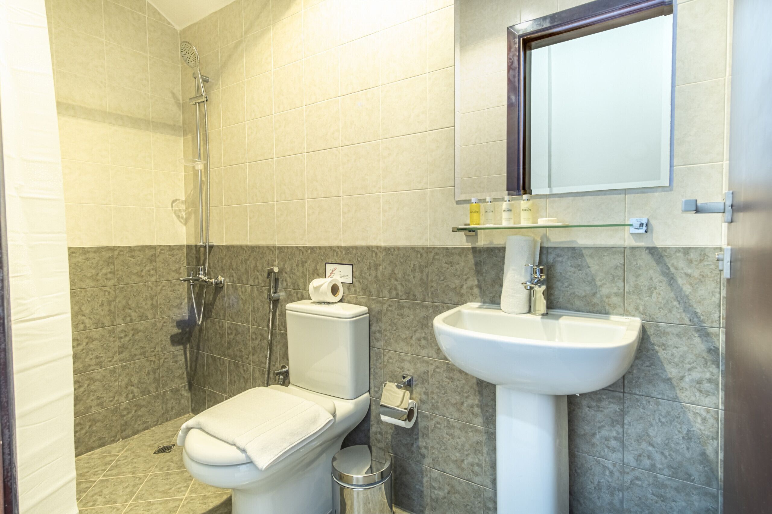 A bathroom with a toilet, shower, sink, and mirror.