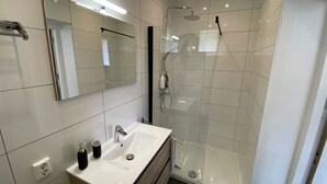 A modern bathroom with a white sink, mirror, and glass shower enclosure. - Modern Studio 3 in Historic Abbey (Cadier en Keer)