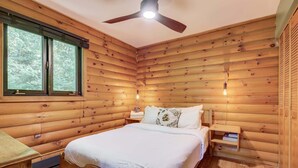 Une chambre dans une cabane en bois, avec un lit, des tables de chevet et un ventilateur de plafond.