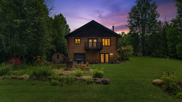 Un chalet rustique en rondins de bois, doté d’un balcon, entouré d’une pelouse et d’un jardin bien entretenus.