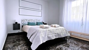 Een moderne slaapkamer met een groot bed, twee nachtkastjes, een hoofdbord met een bladmotief en uitzicht op het buitengebeuren door transparante gordijnen.