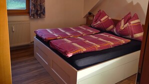 Une chambre à coucher avec un lit, une fenêtre avec des rideaux, un radiateur et un plancher en bois.