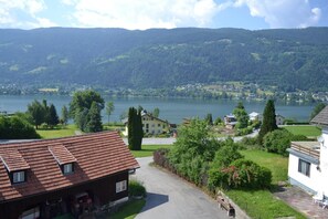 Un quartiere residenziale con una casa dotata di tetto in tegole rosse, vialetto d'accesso e vista su un lago e colline circostanti.