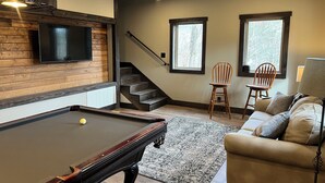 Ein Billardtisch, eine Couch und eine Treppe in einem Raum mit Holzwänden und Fenstern.