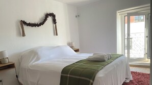 Ein ordentlich gemachtes Bett mit weißen Leinen, einer grün-weißen Karodecke und zwei weißen Handtüchern. An jeder Seite des Bettes steht ein kleiner Nachttisch mit einer Lampe. Über dem Bett hängt eine dekorative Girlande.
