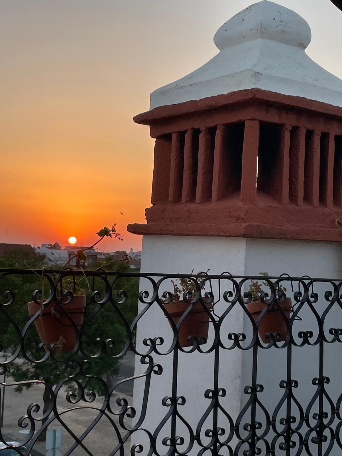 A balcony with a white structure and red columns, overlooking a sunset.