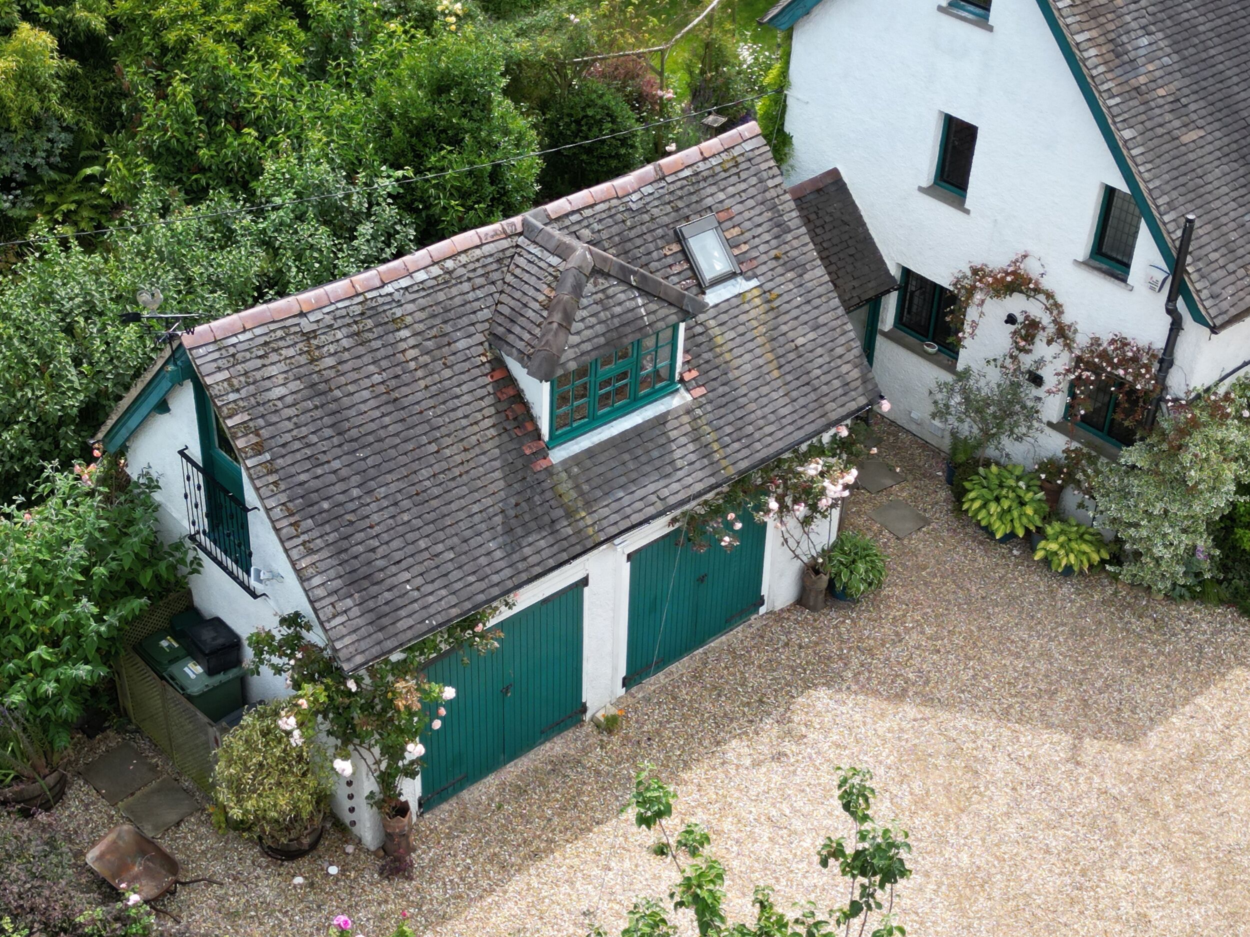 A two-story house with a sloped roof, a green door, and a small garden area with potted plants.