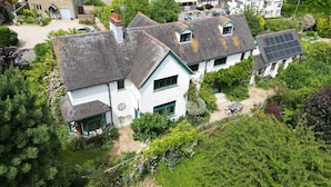 Ein weißes Haus mit grauem Dach, umgeben von üppiger Bepflanzung und einem kleinen Garten.