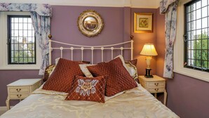 A bedroom with a bed, nightstands, a mirror, and a window with curtains. - White House (Chipping Campden)