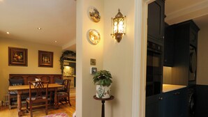 A dining area with a wooden table and chairs, a patterned rug, and a wall-mounted light fixture. - White House (Chipping Campden)