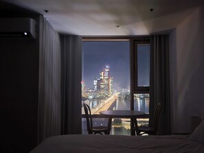 A hotel room with a large window offering a nighttime city view, a bed, and a small table with chairs. - 1#[Mapo Station] Best View! Han River View- Skyline Stay (Seoul)
