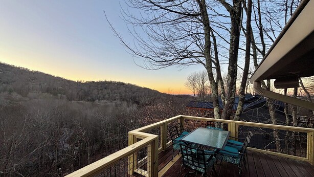 Una terraza de madera con una mesa y sillas, con vista a un área boscosa.
