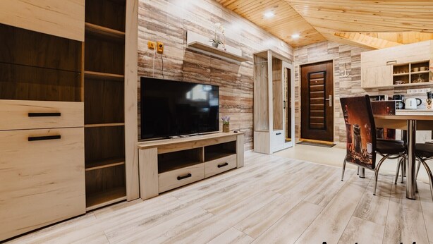 A modern kitchen with wooden cabinetry, a built-in TV, and a dining area with a chair and table. - Noua Oasis BNB with parking (Brașov)