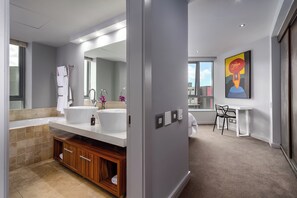 A modern bathroom with a large sink, mirror, and wooden cabinet. There is a small table and chair in the adjacent room. - Perfect Location City Centre - 2-bed apartment with pool and good vibes (Cape Town)