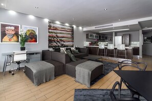 A modern living room with a sectional sofa, a dining table, and a kitchen area in the background. - Perfect Location City Centre - 2-bed apartment with pool and good vibes (Cape Town)