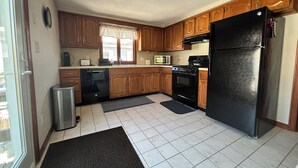 Une cuisine avec des meubles de rangement en bois, un réfrigérateur noir, un four à micro-ondes, une cuisinière et un lave-vaisselle.