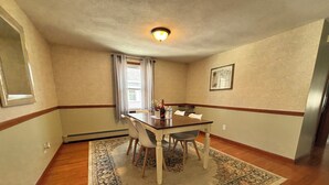 Un coin repas comprenant une table en bois, quatre chaises, un tapis, une fenêtre avec des rideaux et un luminaire au plafond.