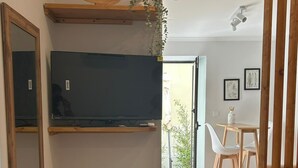 A modern living room with a flat-screen TV, wooden shelves, a mirror, and a dining area with a table and chairs. - Villa Medusa Beach Studios, Seahorse (Parede)