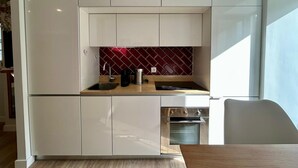A compact kitchen with white cabinets, a red backsplash, and a built-in oven. - Villa Medusa Beach Studios, Seahorse (Parede)