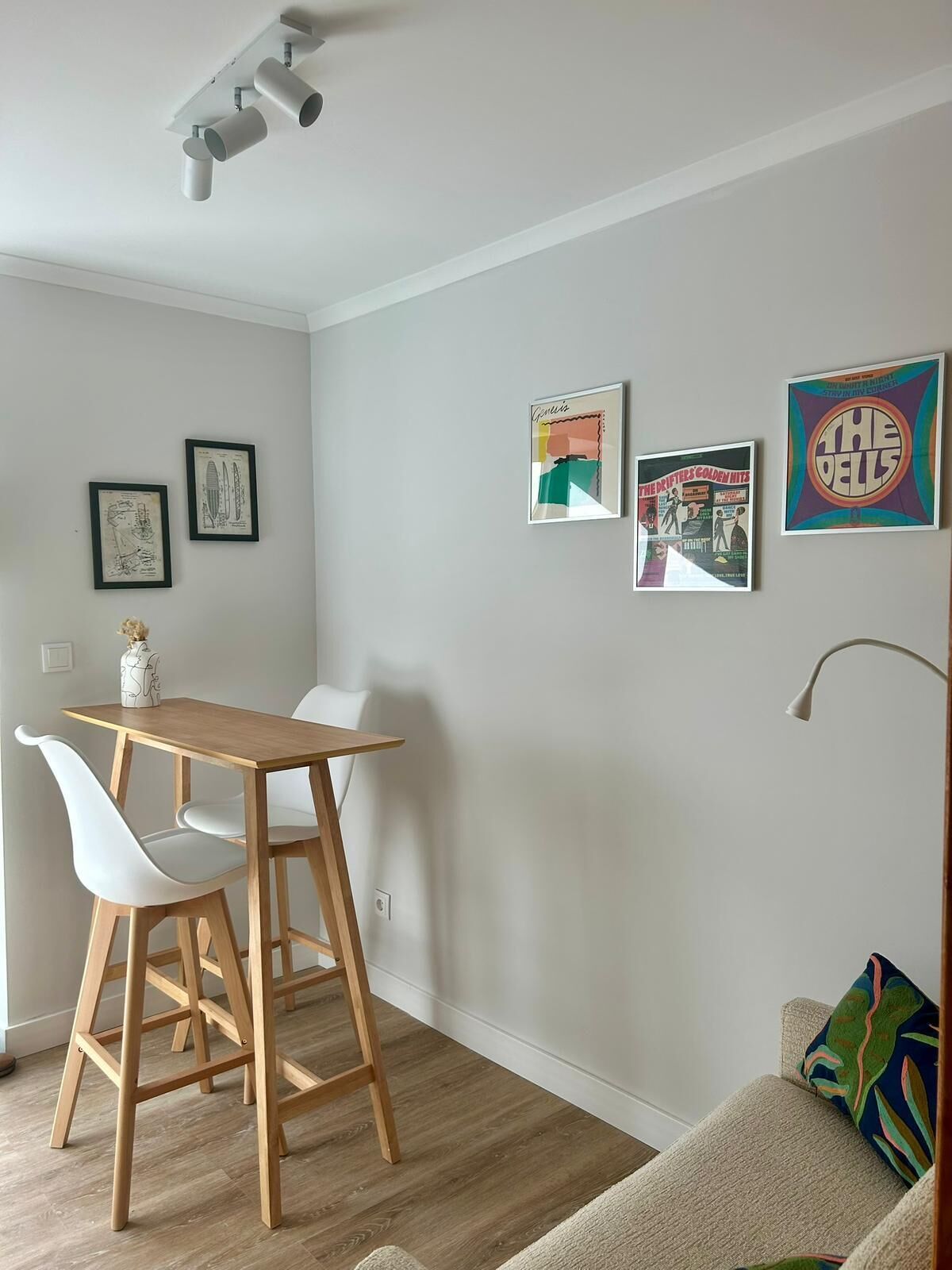 A modern living room with a wooden dining table, white chairs, a beige sofa, and a colorful throw pillow.